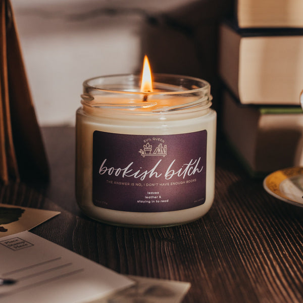 Candle with a 'bookish bitch' label on a table with books and a teacup.
