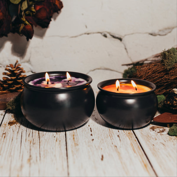 Two black candle holders with lit candles on a rustic wooden surface with dried flowers and pinecones.