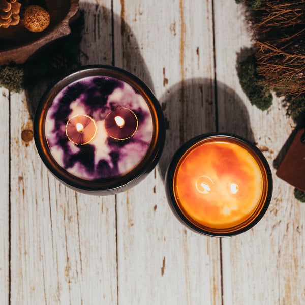 Two lit candles on a wooden surface with decorative elements.