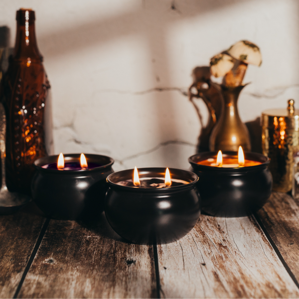 Three lit candles in black holders on a wooden surface with decorative bottles and jars in the background.